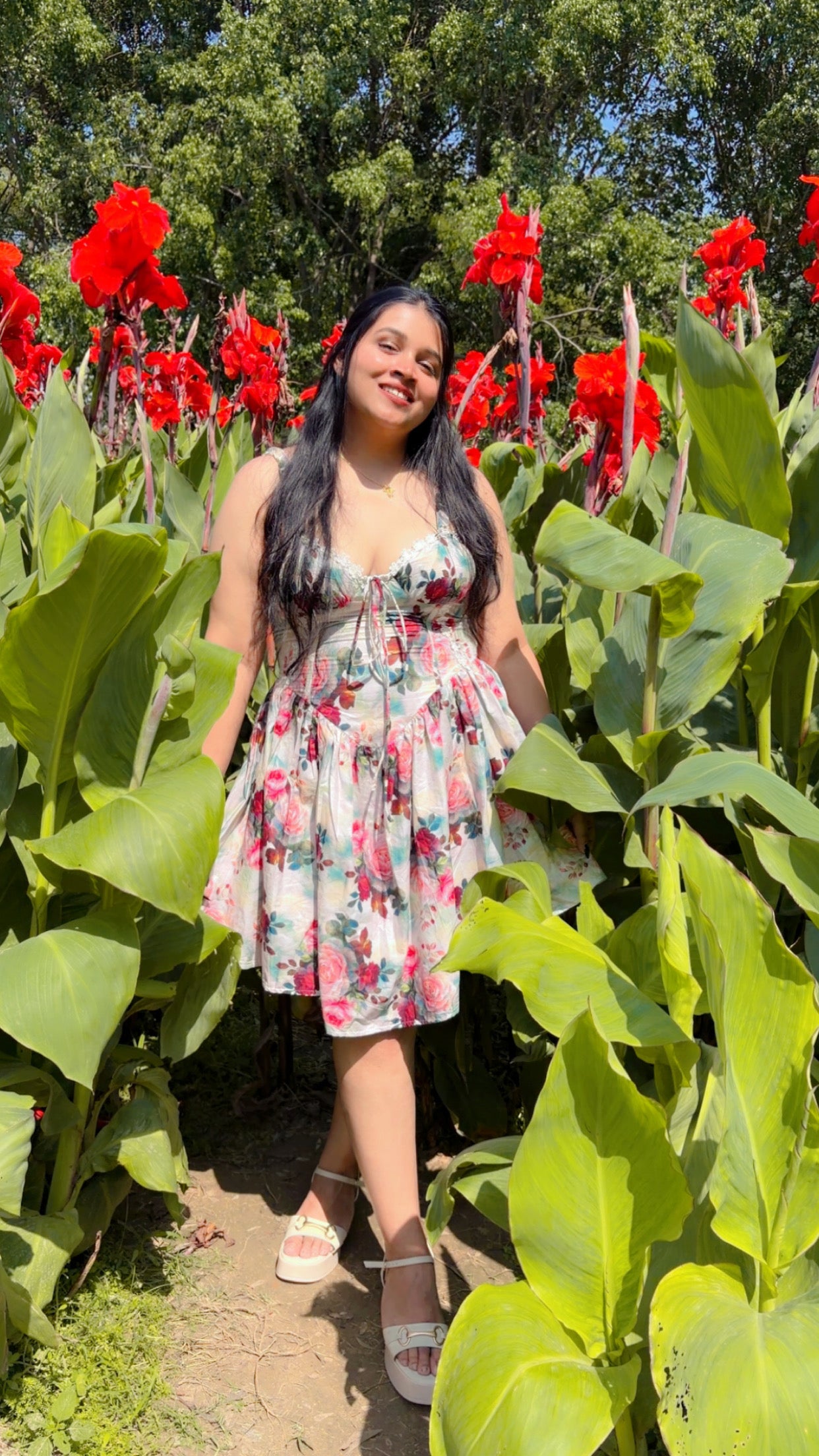 Woman in a floral dress standing among red flowers and green foliage