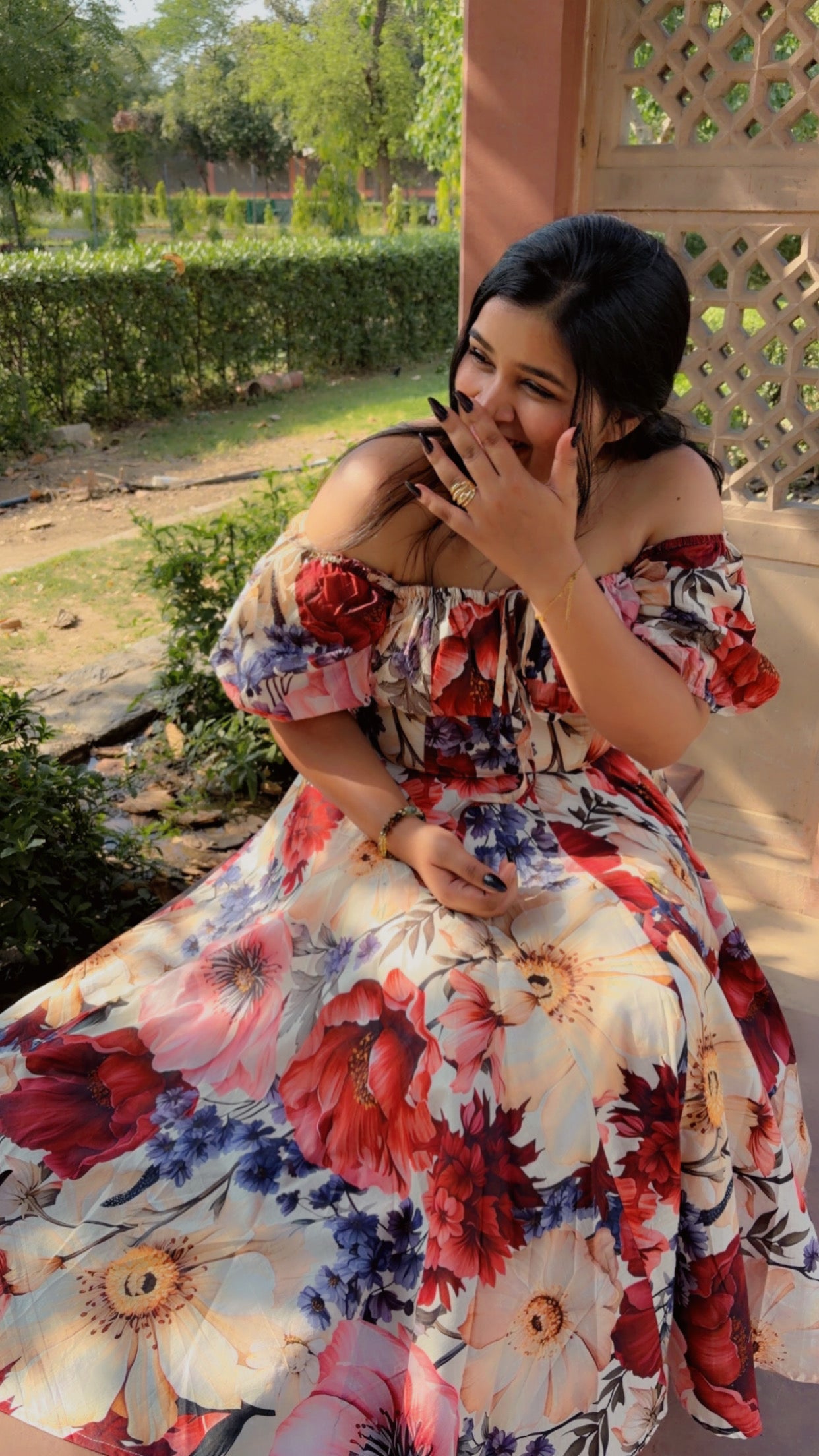 Woman in a floral dress sitting outdoors with greenery in the background