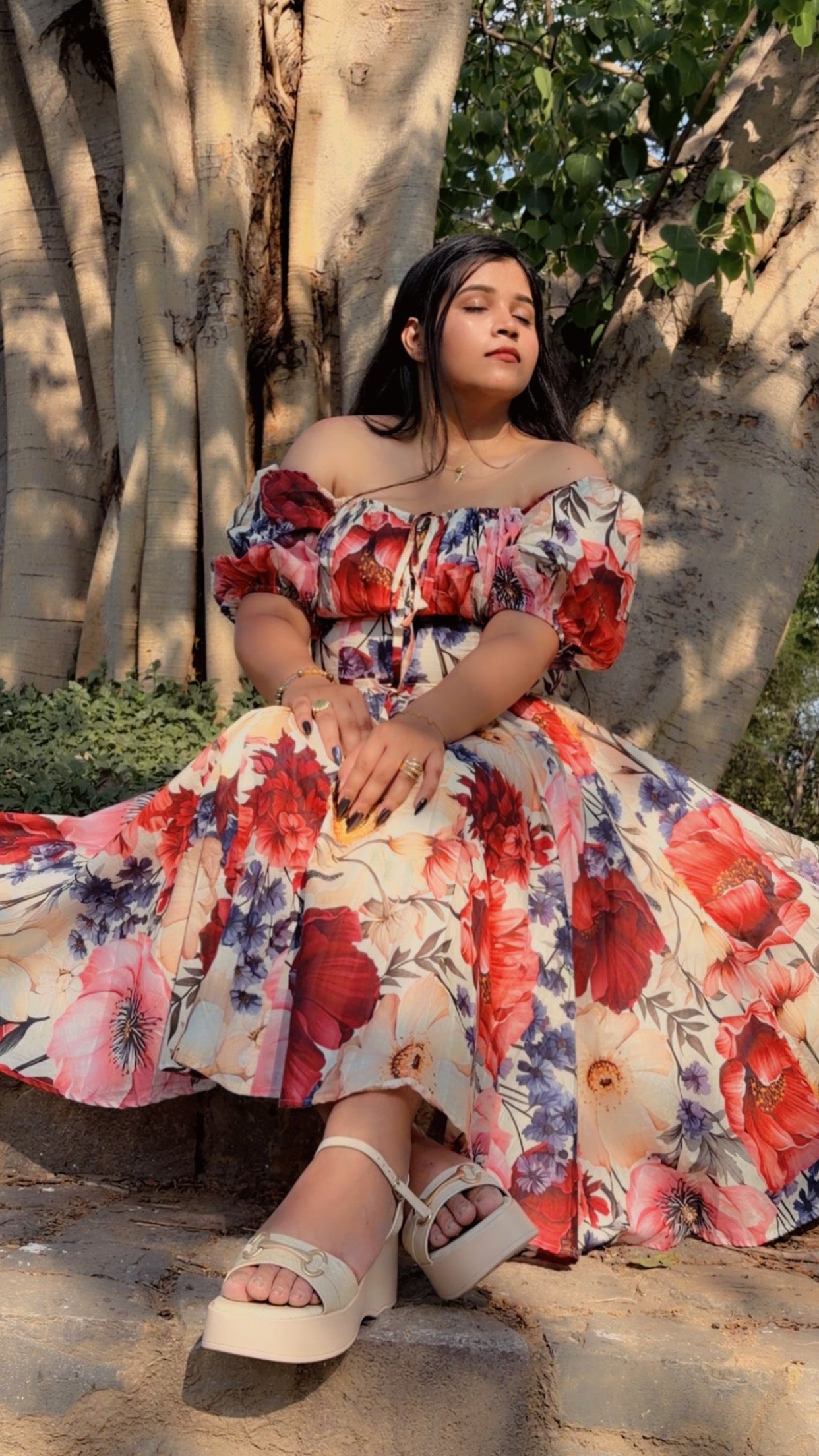 Woman in a floral dress sitting under a tree