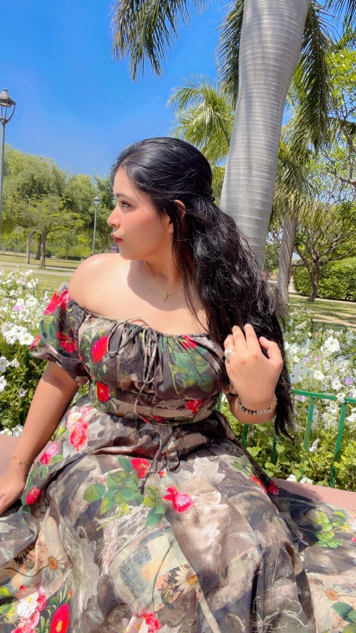 Woman in a floral dress sitting outdoors with greenery and flowers in the background